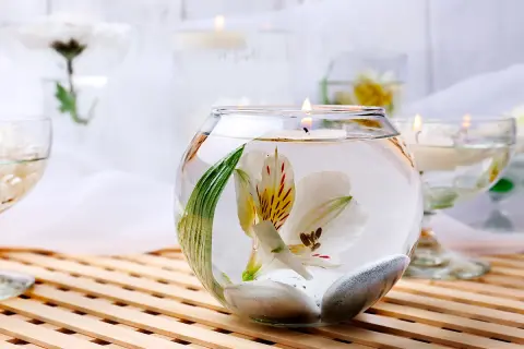 Comment décorer un grand vase en verre transparent : une fleur blanche flottante, des galets et une bougie allumée créent une ambiance zen.