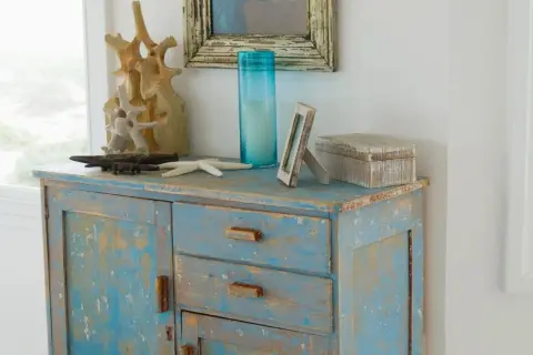 Meuble patiné bleu délavé, orné d'objets marins et d'une boîte décorative.
