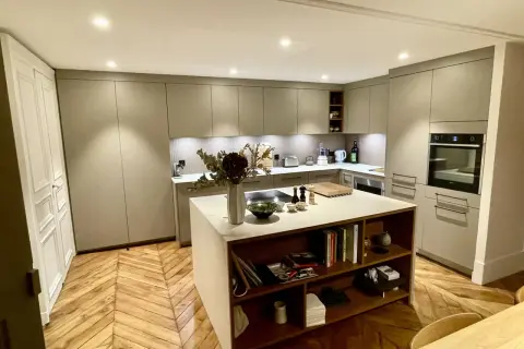 Cuisine moderne avec îlot central, table intégrée, rangements et parquet en chevrons.