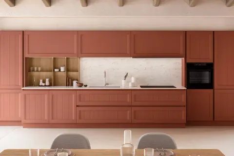 Cuisine moderne avec des armoires couleur terre cuite, un évier, un four et des chaises grises.