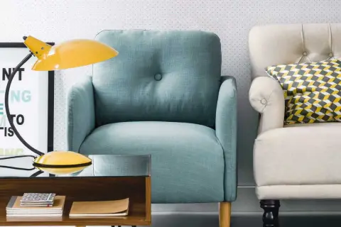 Fauteuil confortable couleur aqua, à côté d'un autre fauteuil crème avec un coussin géométrique. Une lampe jaune et une table basse en bois complètent la scène.