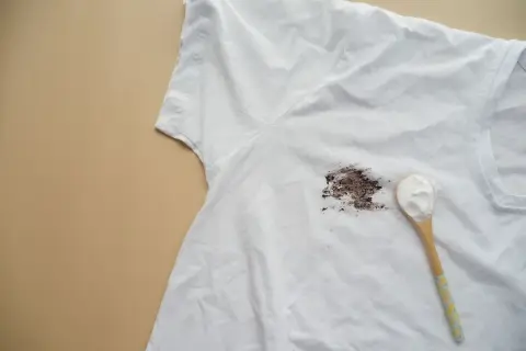 Tache de gras sur un t-shirt blanc, avec une cuillère de poudre blanche prête à enlever la tache de gras sur tissu.
