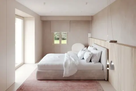 Chambre moderne épurée avec lit blanc, tapis rose et fenêtre donnant sur un jardin.