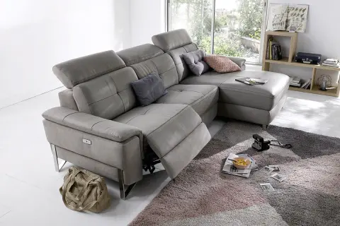 Canapé d'angle gris en cuir, avec repose-pieds déployé. Ce fauteuil relax qui grince est prêt pour un moment de détente.