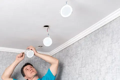 Un homme installe de nouvelles suspensions rondes au plafond, remplaçant les anciens spots.