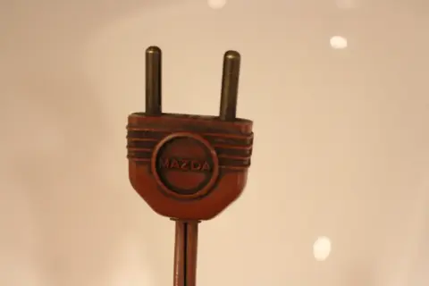 Prise électrique ancienne en bakélite marron avec le logo Mazda. Pour savoir comment reconnaître une lampe Mazda, cherchez cette marque distinctive.