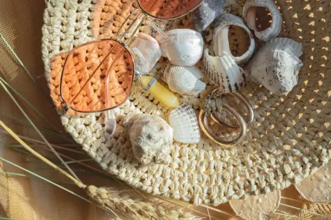 Lunettes de soleil roses, coquillages, bijoux et herbes sèches sur un chapeau de paille.