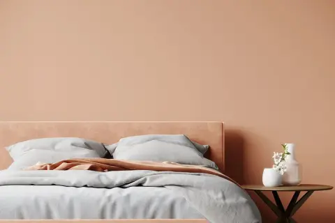 Lit douillet dans une chambre aux tons pêche, une belle idée couleur chambre adulte zen. Draps gris, plaid corail et vase fleuri sur table ronde.