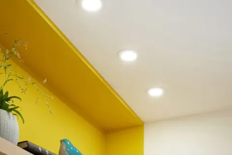 Disposition de spots encastrés au plafond pour une ambiance lumineuse dans la chambre, éclairant joliment les étagères jaunes.