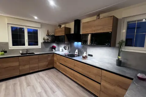 Cuisine moderne avec meubles en bois, plan de travail gris et hotte noire.