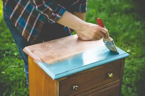 Une personne ponce un meuble vernis pour le repeindre en bleu sarcelle.