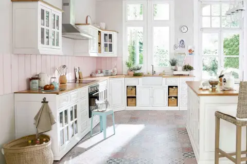 Une cuisine blanche style campagne chic, lumineuse avec ses grandes fenêtres, son plan de travail en bois et son sol aux motifs colorés.