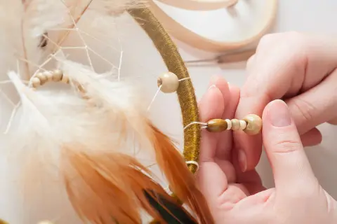 Mains assemblant un attrape-rêves, ajoutant des perles en bois pour une touche naturelle. Idées pour que faire avec des perles en bois.
