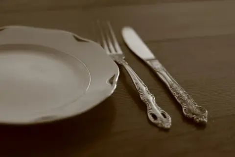 Une assiette blanche et des couverts en argent ornés, prêts pour un repas. Apprenez comment nettoyer des couverts en argent pour qu'ils brillent.