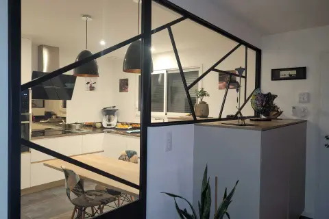 Une cuisine moderne avec une cloison lumineuse en verre et métal noir, séparant l'espace repas de la cuisine.