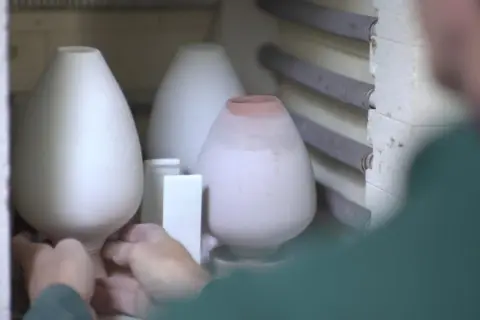 Mains plaçant délicatement des pièces de céramique au four pour leur cuisson.