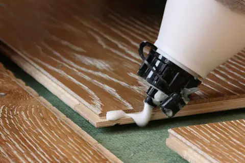 Application de colle à bois sur des lames de parquet. La colle blanche coule de l'embout d'une bouteille sur le bois.