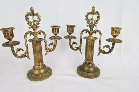 Deux candélabres en bronze doré, ornés de guirlandes et de cannelures, illustrent comment reconnaître un chandelier ancien par leur style et leur patine.