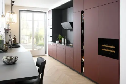 Cuisine moderne avec des armoires bordeaux allant jusqu'au plafond, un îlot central gris, et une grande fenêtre lumineuse.
