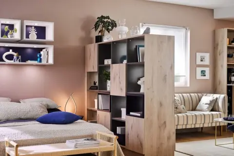 Chambre et salon séparés par une étagère modulable, avec lit douillet et canapé rayé.