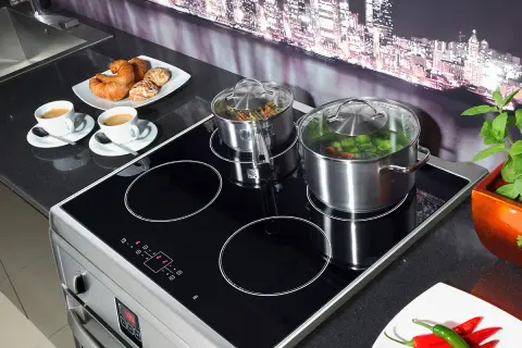 Plaque à induction avec deux casseroles, tasses de café et viennoiseries.