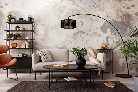 Salon au **couleur mur style industriel**, avec canapé gris, fauteuil orange, étagères noires et table basse.