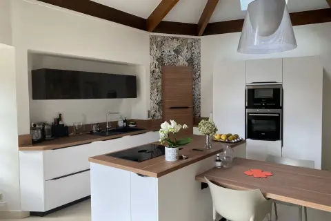 Cuisine moderne avec des meubles blancs et un **crédence et plan de travail assortis** en bois. Une orchidée blanche décore l'îlot central.