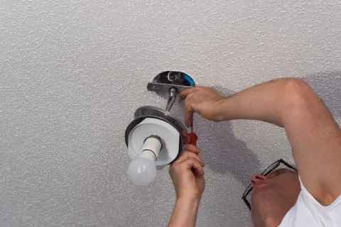 Un homme installe un lustre au plafond, utilisant un tournevis pour fixer le luminaire.