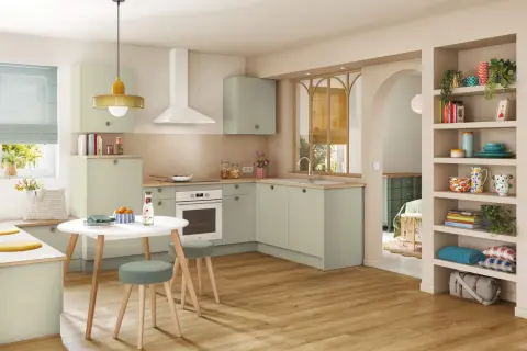 Cuisine moderne et colorée avec des meubles verts, une table ronde et des étagères décorées.