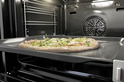 Une pizza garnie sur une plaque dans un four pyrolyse Siemens. La pizza est prête à être cuite.