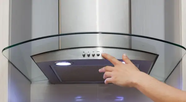 Main d'une personne appuyant sur le bouton d'une hotte recyclage ou évacuation moderne en acier inoxydable avec un éclairage intégré.