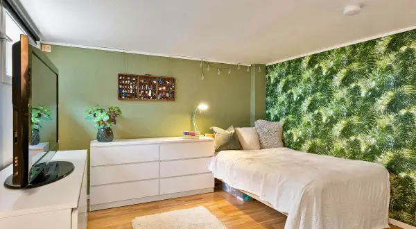 Chambre avec mur végétal, lit blanc, commode et télévision.
