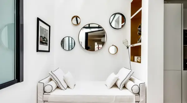 Plusieurs miroirs ronds de tailles variées sont accrochés sur un mur blanc au-dessus d'un canapé blanc.
