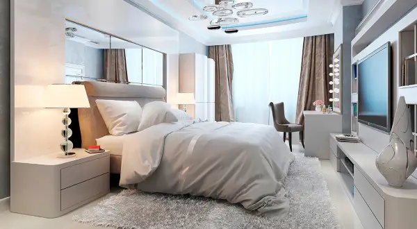Chambre moderne avec un grand lit douillet, un miroir au dessus du lit reflétant le plafond design et une télévision murale.