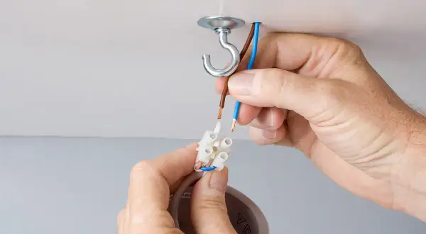 Mains électriques connectées pour changer un lustre. Un crochet au plafond supporte le nouveau luminaire.