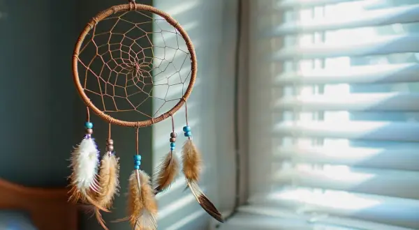 Attrape-rêves artisanal avec plumes et perles bleues, suspendu devant des stores.