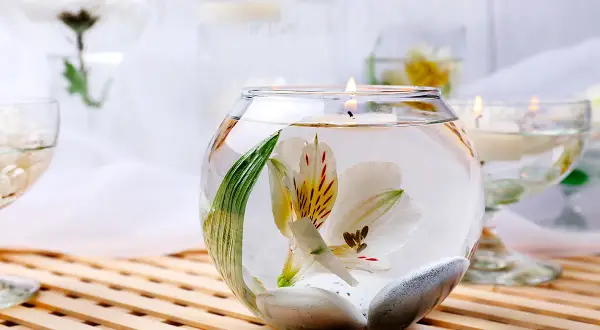 Comment décorer un grand vase en verre transparent : une fleur blanche flottante, des galets et une bougie allumée créent une ambiance zen.