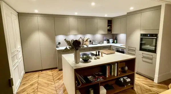 Cuisine moderne avec îlot central, table intégrée, rangements et parquet en chevrons.