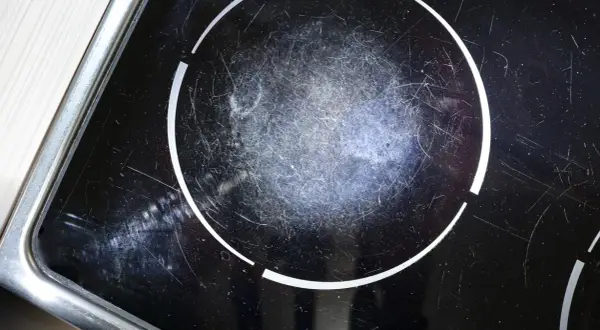 Gros plan sur une plaque à induction noire, marquée par de nombreuses rayures sur la zone de cuisson.