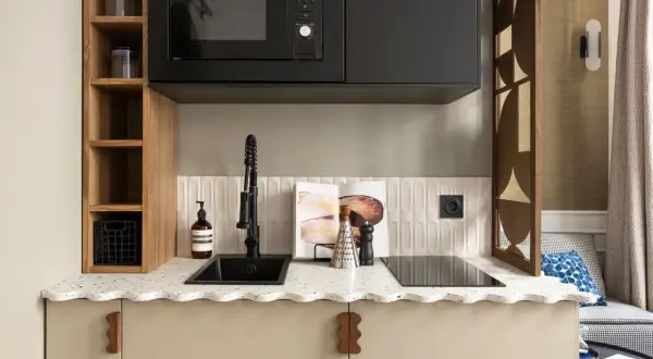 Petite cuisine moderne avec évier noir, plaque de cuisson, micro-ondes et étagères en bois.