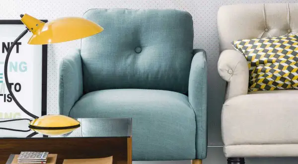 Fauteuil confortable couleur aqua, à côté d'un autre fauteuil crème avec un coussin géométrique. Une lampe jaune et une table basse en bois complètent la scène.