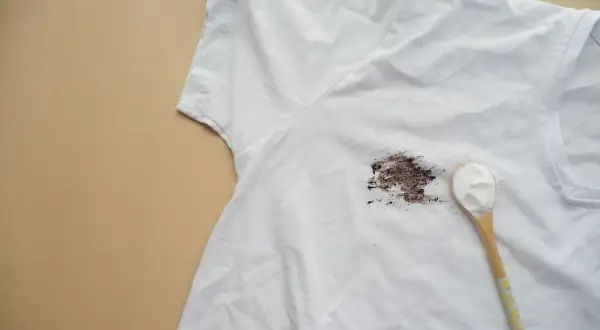 Tache de gras sur un t-shirt blanc, avec une cuillère de poudre blanche prête à enlever la tache de gras sur tissu.