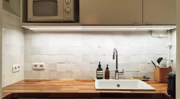 Cuisine blanche épurée avec crédence en zellige texturé, plan de travail en bois, évier et robinetterie modernes.
