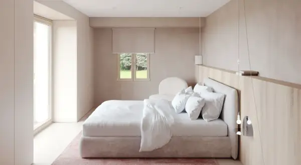 Chambre moderne épurée avec lit blanc, tapis rose et fenêtre donnant sur un jardin.