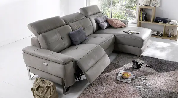 Canapé d'angle gris en cuir, avec repose-pieds déployé. Ce fauteuil relax qui grince est prêt pour un moment de détente.