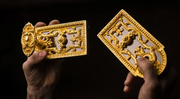 Mains tenant des ornements dorés, peut-être du bronze ou du laiton, aux motifs complexes.