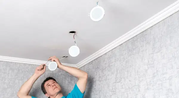 Un homme installe de nouvelles suspensions rondes au plafond, remplaçant les anciens spots.