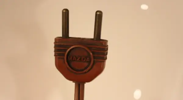 Prise électrique ancienne en bakélite marron avec le logo Mazda. Pour savoir comment reconnaître une lampe Mazda, cherchez cette marque distinctive.