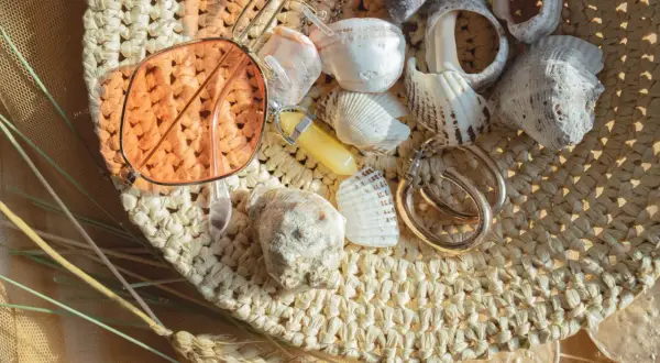 Lunettes de soleil roses, coquillages, bijoux et herbes sèches sur un chapeau de paille.