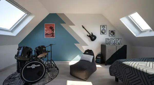 Chambre d'ado avec batterie, guitare électrique, pouf et lit décoré.